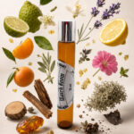 frasco de perfume roll on em vidro âmbar com tampa cromada em posição vertical rodeado por pedaço de âmbar cedro laranja gomo de tangerina limão lírio lavanda