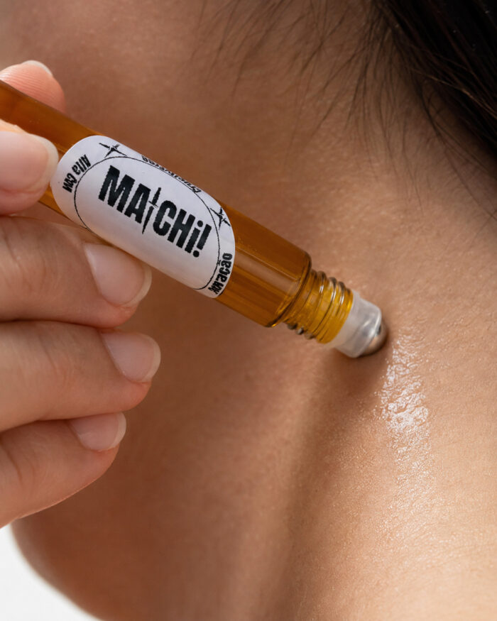 dedos polegar e indicador aplicando perfume com frasco cilíndrico feito de vidro com ponta aplicadora redonda de aço deslizante no pescoço feminino