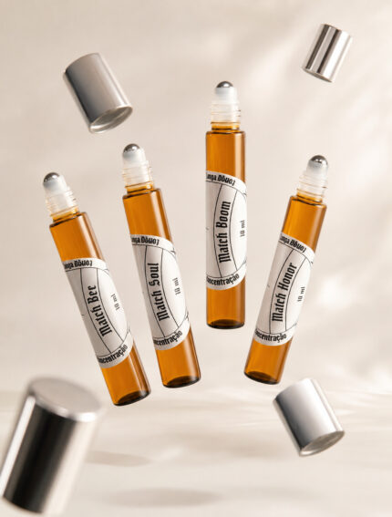 Quatro frascos cilíndricos de perfume de bolsa feitos com vidro âmbar e com pontas de aço deslizantes com rótulos brancos levitando lado a lado e tampas prateadas orbitando ao redor