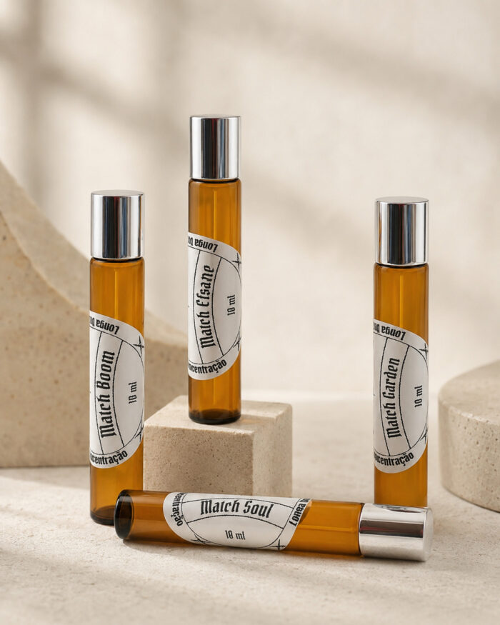 três frascos cilíndricos de perfume feitos em vidro âmbar com tampas prateadas com rótulos brancos redondos na posição vertical lado a lado sob pedra de granito e um frasco na horizontal