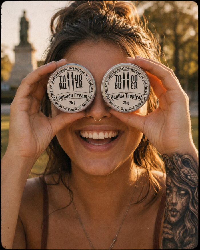 Mulher sorridente segura diante dos olhos as duas latinhas de alumínio do Kit Ikii, com rótulos brancos redondos Matchii Cupuaçu Cream e Vanilla Tropical, em ambiente externo com tatuagem visível no braço.