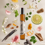 perfume feminino no frasco cilíndrico em vidro âmbar com tampa cromada com rótulo branco redondo match una com fatia de limão rosa fatia de laranja fava tonka lírio cravo ao redor do frasco